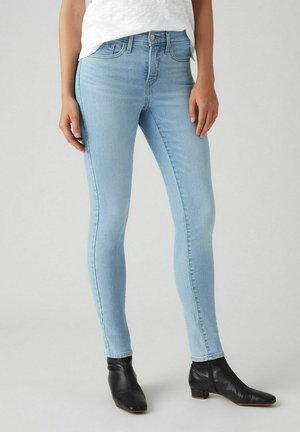 Jeans skinny de color azul claro, hechos de denim, con una cinturilla estándar, cuatro bolsillos y una textura suave, combinados con botines negros.