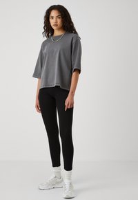 T-shirt gris surdimensionné à manches courtes, associé à un legging noir et des baskets blanches. Présente une coupe décontractée et un détail de collier en chaîne.