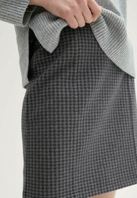 Jupe à carreaux gris avec une coupe ajustée, fabriquée en tissu texturé. Couture visible le long de l'ourlet et taille haute avec un haut en tricot doux.