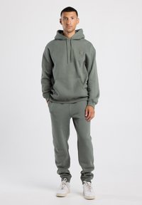 Felpa verde chiaro e pantaloni della tuta coordinati realizzati in tessuto morbido. Presenta una tasca a marsupio, un cappuccio con coulisse e polsini a coste.