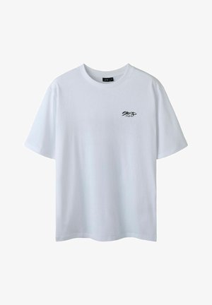 T-shirt en coton blanc avec un col rond et des manches courtes. Présente un petit graphisme en texte noir sur la zone gauche de la poitrine. Texture lisse.