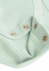 Tessuto a coste verde chiaro con bottoni a pressione metallici. Texture liscia, bordi arrotondati e dettagli di design a strati visibili vicino ai bottoni.