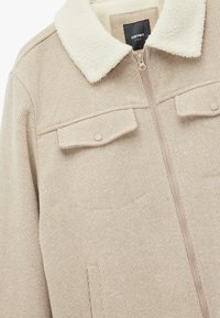 Beige stribet jakke med en cremet sherpa-krave, lynlås foran og to brystlommer med trykknapper. Blød tekstur og afslappet design.