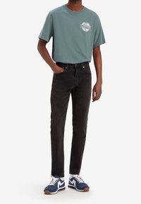 Camiseta de algodón gris con logo, jeans de mezclilla negros y zapatillas azules con acentos blancos. El conjunto presenta un ajuste relajado y un diseño clásico.