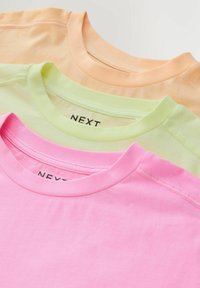 Trois t-shirts en coton soigneusement empilés, aux couleurs pastel rose, vert et orange, avec des encolures arrondies et des étiquettes de marque visibles à l'intérieur des cols.
