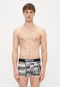 Cuecas boxeadoras pretas e brancas com padrão gráfico repetido, apresentando um cós elástico com a marca "DIESEL". Tecido macio.