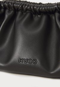 Pochette in pelle nera con texture arricciata; presenta il logo "HUGO" embossato in basso a destra. Finitura liscia e opaca.