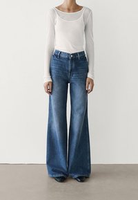 Top bianco a maniche lunghe con scollatura a barca abbinato a jeans azzurri a vita alta e gamba larga, con lavaggio sbiadito e tasche frontali.