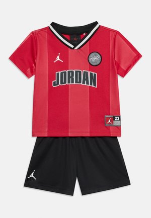 Tenue de basketball rouge et noire comprenant un haut rouge Jordan à manches courtes avec col noir et un short noir avec le logo Jordan.
