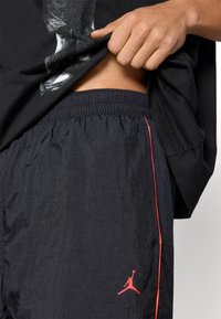 Μαύρα σορτς από ελαφρύ, υφασμάτινο ύφασμα με υφή, διαθέτουν ελαστική μέση και κόκκινη ρίγα ως διακοσμητικό, με μικρό κόκκινο λογότυπο στο πλάι.