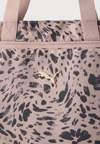 Μπεζ τσάντα με μαύρα αφηρημένα στίγματα, χρυσό λογότυπο Puma και μπεζ υφασμάτινες λαβές ραμμένες στην κορυφή.