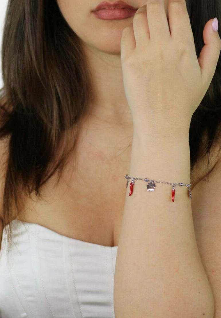 Bracciale in argento con charm a forma di peperoncino rosso, link delicati e un piccolo charm a forma di quadrifoglio. Tono della pelle visibile nella zona del polso.