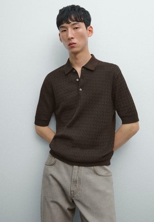 Brown knitted polo shirt with short sleeves, featuring a textured pattern, a collar, and three-button placket. Paired with light gray jeans.