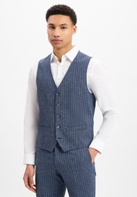 Blau gestreifter Weste aus strukturiertem Stoff, mit V-Ausschnitt, fünf Knöpfen und zwei Seitentaschen, über einem weißen Hemd getragen.