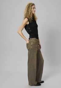 Czarny bezrękawnik z metalicznymi srebrnymi akcentami po bokach, zestawiony z szerokimi brązowymi dżinsami. Materiał wydaje się miękki o gładkiej fakturze.