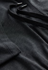 Zwarte stof met een zachte textuur, voorzien van twee donkere trekkoorden met metalen uiteinden, die een casual kledingontwerp tonen.