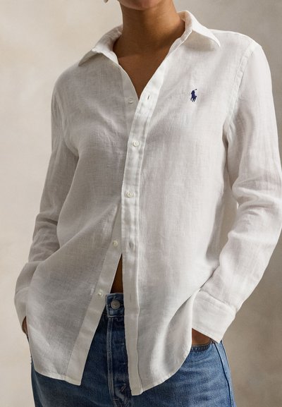 Λευκό πουκάμισο από λινό με κουμπιά και κλασικό γιακά, διακοσμημένο με κεντημένο λογότυπο· συνδυασμένο με ψηλόμεσο τζιν τζιν. Μαλακή υφή, άνετη εφαρμογή.