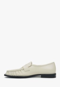 Leather loafers in light cream with a smooth texture, featuring a rounded toe, pleated detailing, and a low black heel.