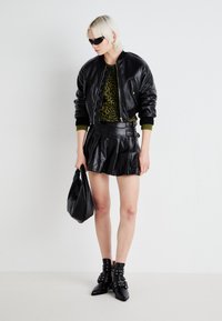 Chaqueta bomber de cuero negra sobre una blusa verde con estampado de leopardo, combinada con una falda corta plisada negra, botas negras hasta el tobillo y un bolso negro.