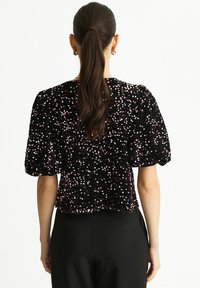 Black sequined top with puff sleeves, featuring a textured surface and scattered pink accents, paired with black high-waisted pants.
