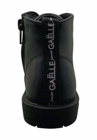Stivaletto in pelle nera con zip laterale, suola piatta e linguetta in tessuto con la scritta "GAËLLE junior" in bianco. Texture liscia e linee pulite.