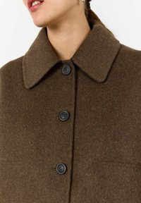 Brown wool coat featuring a large collar, four black buttons, and textured fabric. Includes two front pockets with a smooth finish.