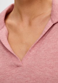 Rosa texturerad tröja med V-ringning och krage. Mjukt tyg med en ljus, melerad look. Fokusera på designen av halsringningen och kragen.