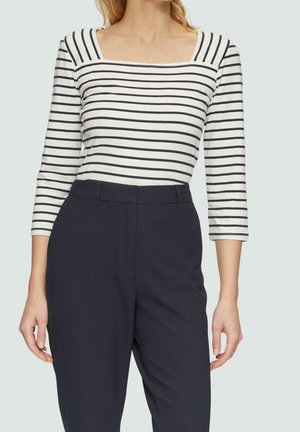 Femme portant un haut blanc rayé bleu marine à encolure bateau avec manches trois-quarts et pantalon taille haute bleu marine foncé.