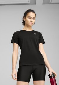 Camisa atlética negra de manga corta con cuello redondo y logo. Combinada con pantalones cortos ajustados negros y sosteniendo una botella de agua rosa. Textura suave.