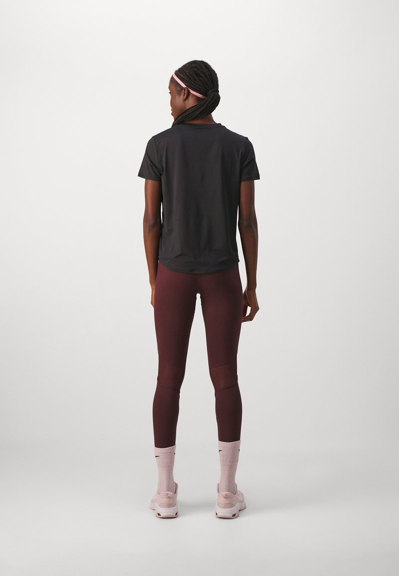 Schwarzes kurzärmliges Sportoberteil und dunkle burgunderfarbene Leggings mit Mesh-Einsätzen, kombiniert mit hellrosa Socken und Schuhen, von hinten betrachtet.