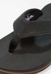 Zwarte flip-flop met een getextureerde rubberen zool, synthetisch bovenwerk en geweven nylonband; heeft een geperst merknamen op de band.