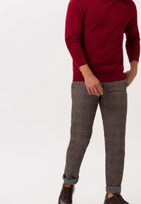 Czerwony sweterek z prążkowanej dzianiny połączony z dżinsami w kratę w odcieniach szarości, brązu i czerwonych akcentach. Brązowe sneakersy z podwiniętymi nogawkami spodni.