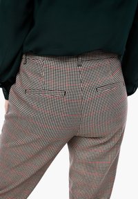 Rutig byxor med svart och vit hounds-tooth-mönster och röda detaljer, med medelhög midja och två bakfickor. Texturerat tyg.