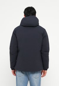Marineblå dunjakke med høj krave og hætte, der har elastiske manchetter og en glat tekstur. Bagside viser minimal detaljering og rene linjer.