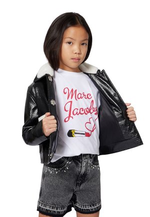 Veste en simili cuir noir avec col en fausse fourrure blanc ; t-shirt blanc avec broderie rouge et graphique ; short en denim noir avec des accents en strass.