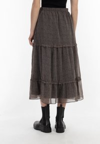 Abito nero a strati, trasparente, con piccoli motivi floreali, vita elastica e una silhouette fluida. Indossato con stivali neri alla caviglia.