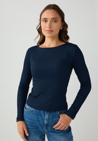 Navy lange mouw ribbel top met een ronde hals, getailleerd ontwerp en een gladde textuur, gecombineerd met lichtblauwe denim jeans.