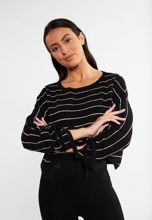 Fekete csíkos pulóver arany kiegészítőkkel, puha anyag, laza fazon, ballonujjak, csuklón megkötős, cropped hosszúság, fekete leggings-szel párosítva.