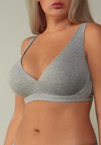 Lichtgrijze, zachte stoffen bralette met een diepe halslijn en brede bandjes. Glad textuur en minimalistisch ontwerp, met een label op de band.