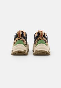 Baskets épaisses avec semelles beiges, accents vert au niveau du talon et dessus à impressions animales variées, vues de dos sur fond blanc.