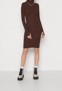 Brun långärmad passformsklänning med hög krage och tumhål, i kombination med beigefärgade och svarta snörda ankelskor med tjock sula.