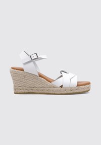 Sandalia de cuña blanca tipo espadrille con suela de yute trenzado, correas cruzadas, hebilla ajustable en el tobillo y plantilla marrón suave.