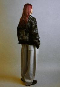 Överdimensionerad svart och grå mönstrad tröja med en texturerad yta, i kombination med ljusgrå vida sweatpants och svarta skor.