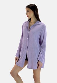 Lyselilla skjorte med knapper, lavet af tekstureret stof. Har en krave, lange ærmer og sideslids, der giver en afslappet pasform.