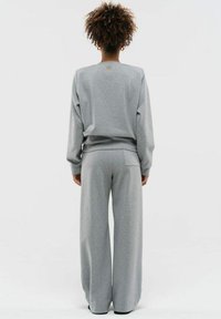 Grijze bijpassende sweatshirt en wijde broek gemaakt van zachte stof, met ribgebreide manchetten en een klein logo op de halslijn.