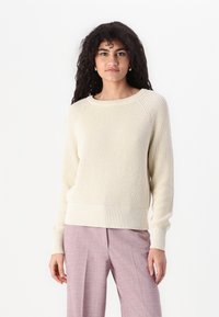 Lys beige ribbestrikket genser med rund hals, lange ermer og teksturert stoff. Kombinert med lyse rosa skreddersydde bukser.