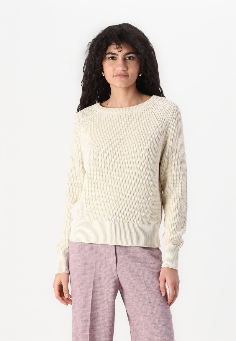 Lys beige ribbestrikket genser med rund hals, lange ermer og teksturert stoff. Kombinert med lyse rosa skreddersydde bukser.
