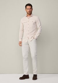 Camisa de manga larga rosa clara con dobles bolsillos en el pecho, diseño de botones en la parte delantera, combinada con pantalones de color claro y zapatos marrones con cordones.