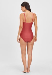 Maillot de bain une pièce rouge avec une texture côtelée, des bretelles réglables et une coupe médiane au dos. Tissu lisse avec un design ajusté.