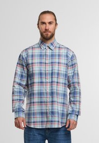 Koszula z długim rękawem w kratę w odcieniach niebieskiego, zielonego, czerwonego i białego. Posiada kołnierzyk zapinany na guziki oraz guziki z przodu, ma luźny krój i lekko zaokrąglony dół.